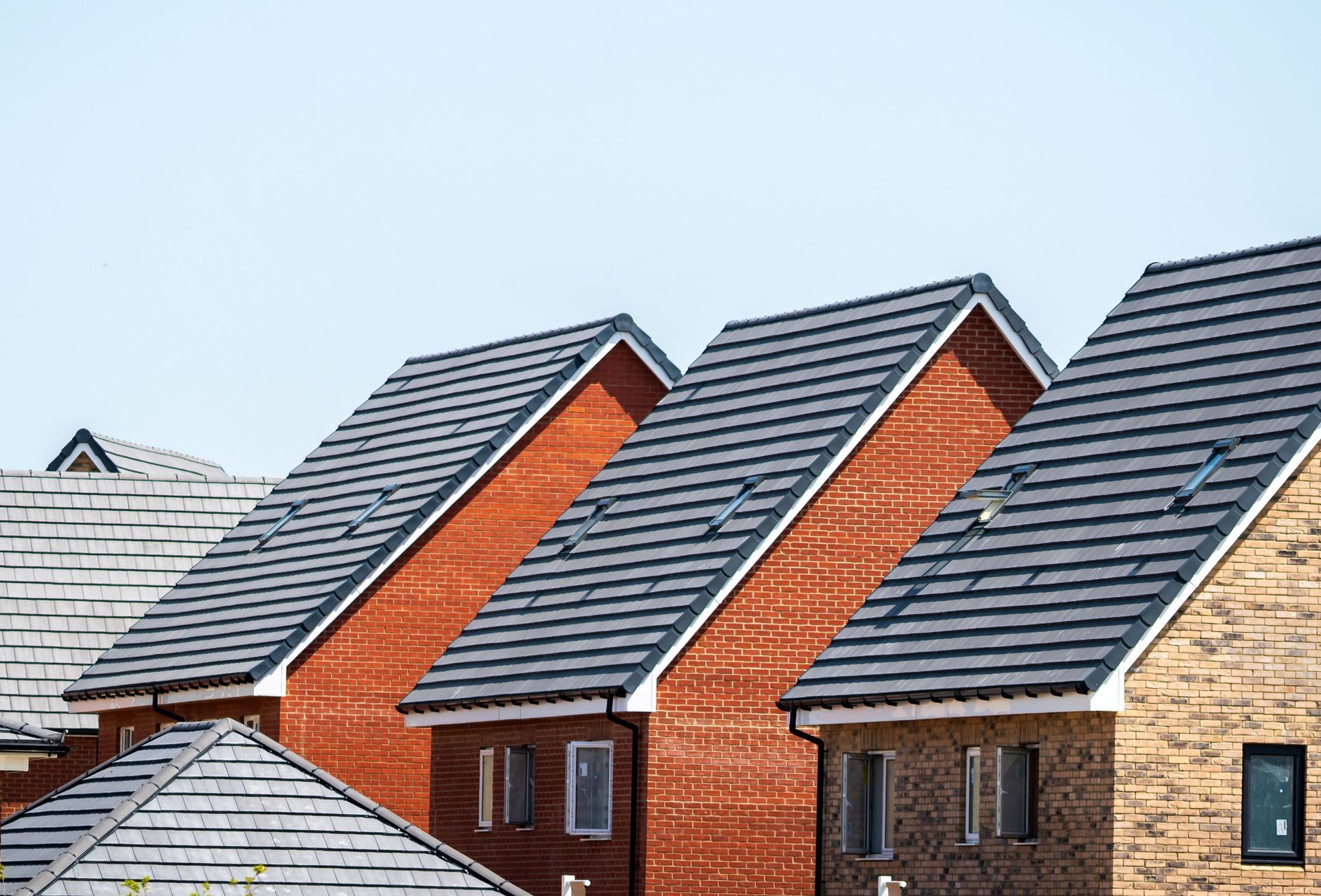 Row of modern brick houses with dark gray roofs and dormer windows under a clear sky