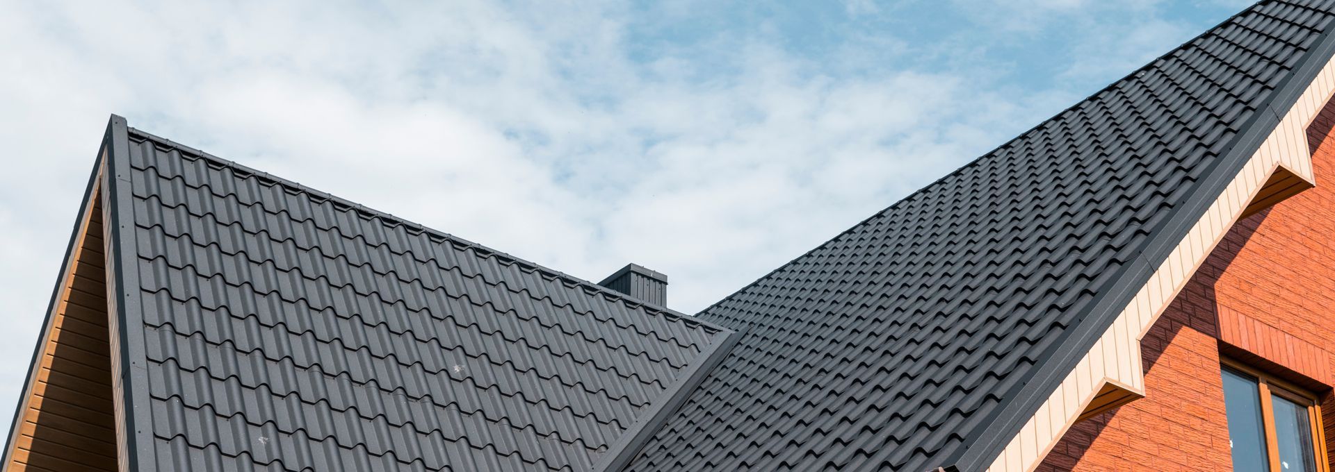 Dark gray tiled house roof with orange brick walls against a cloudy sky