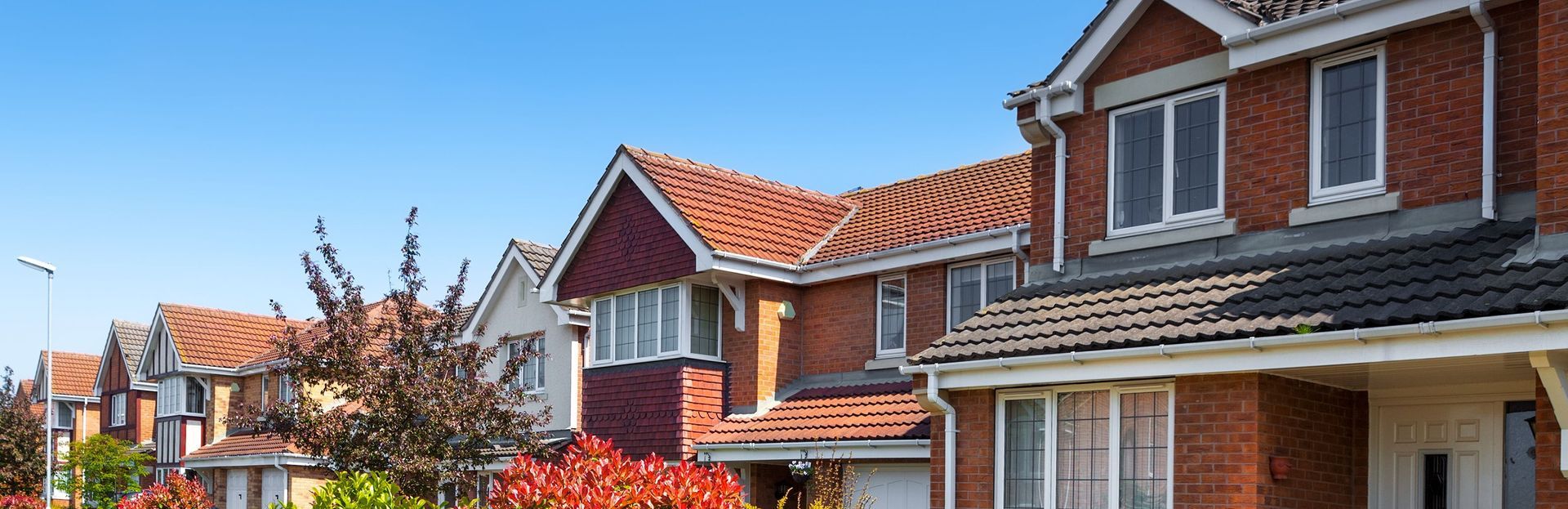 Row of red-brick suburban houses with orange tiled roofs under a clear blue sky