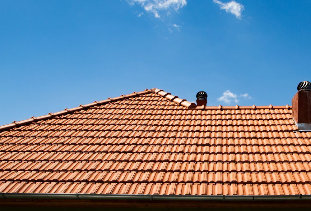Terracotta roof tiles against a bright blue sky with a few clouds