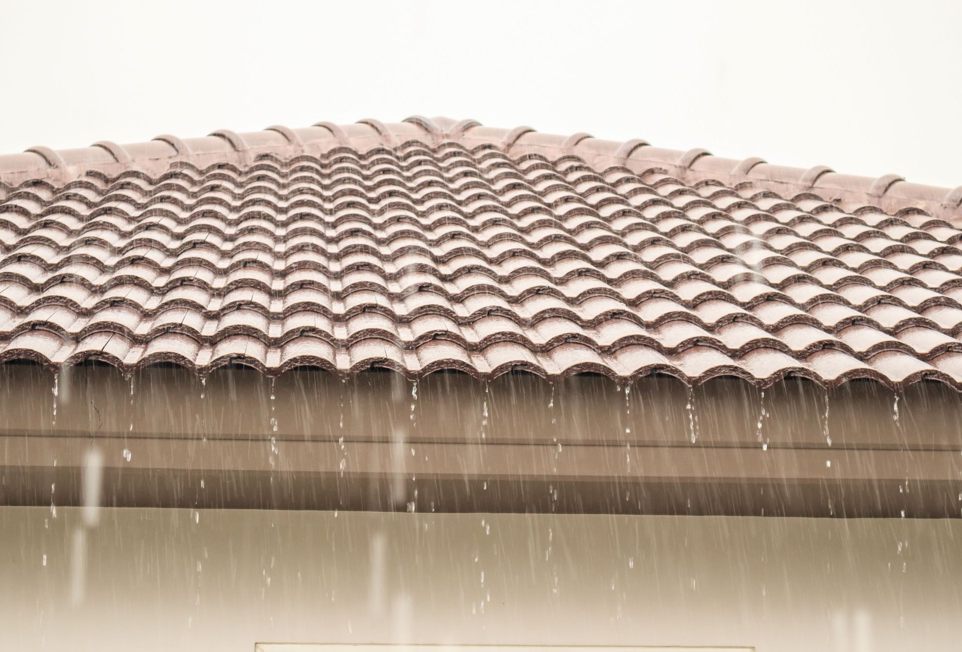 Rain falling on a terracotta-tiled roof with water streaming off the eaves