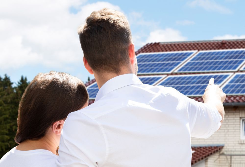 Two people pointing at rooftop solar panels on a sunny day