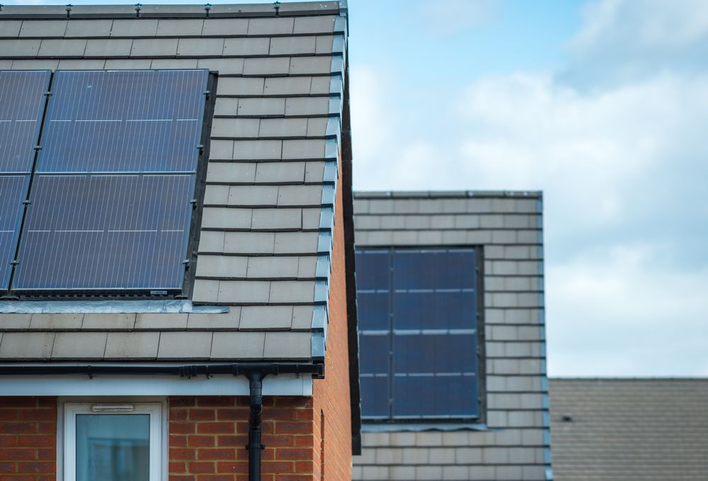 Two rooftops with solar panels against a partly cloudy sky