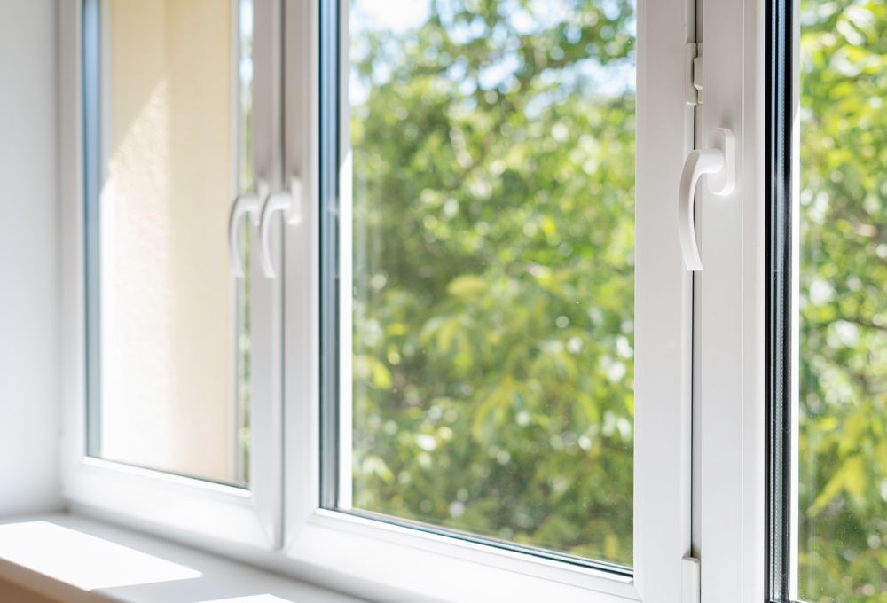 White window frames with two open windows overlooking green trees outside.
