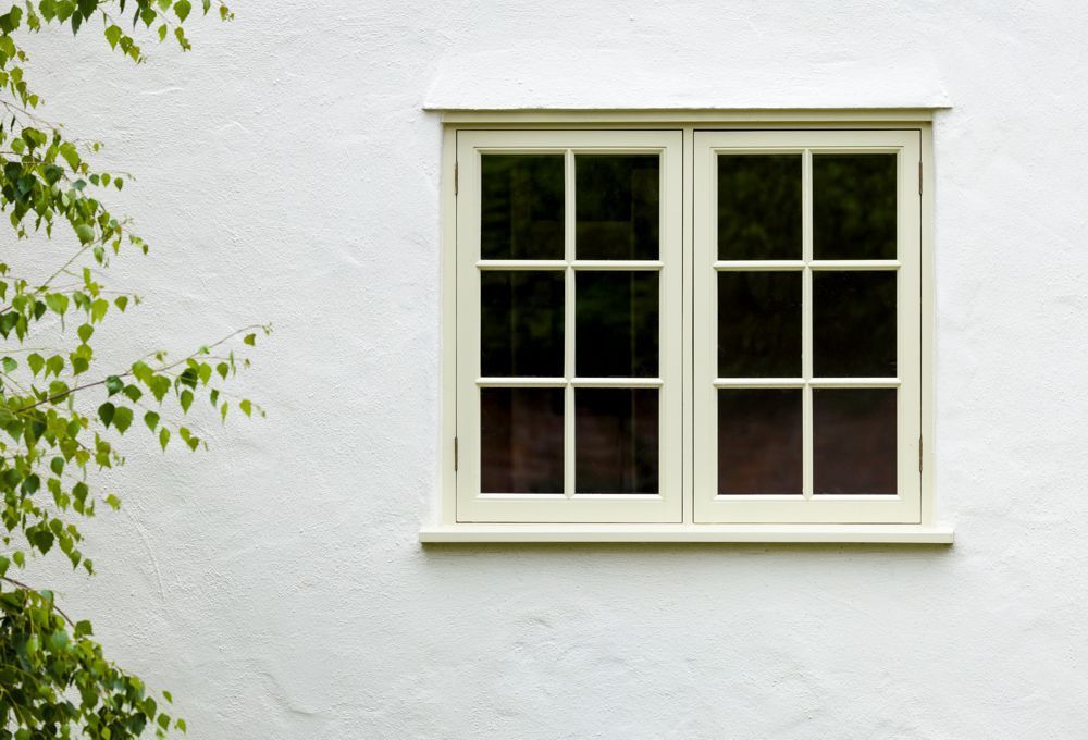White stucco wall with a small cream-framed window and green leaves at the left edge