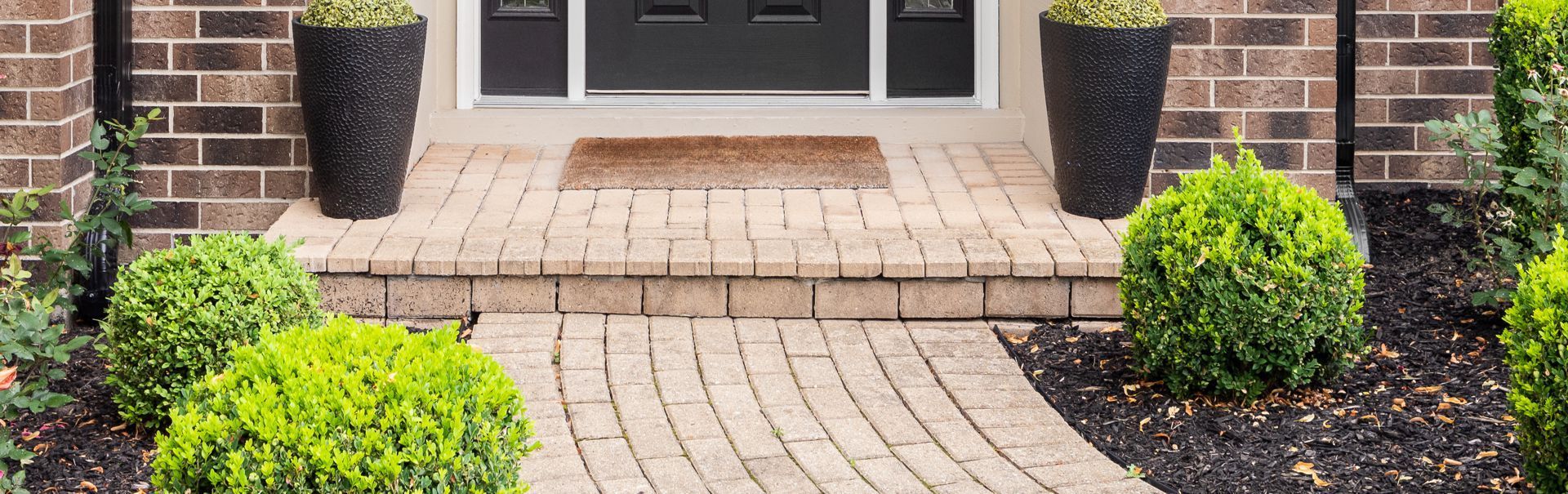Brick house entryway with curved paver walkway and neatly trimmed green shrubs