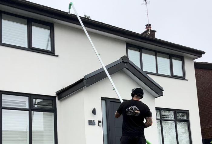 Person using a long pole to inspect a two-story house roof and upper windows