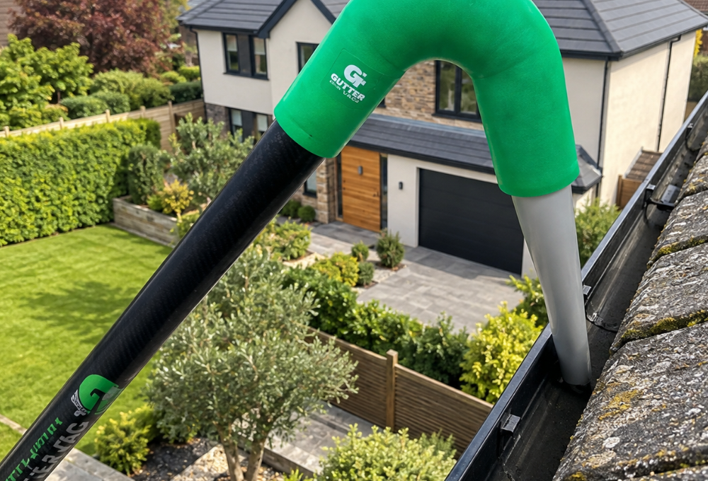 Green and black gutter vacuum hose cleaning a modern house roof gutter above a suburban driveway