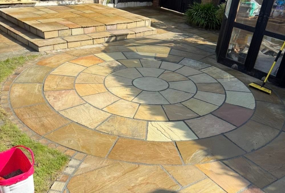 Circular stone patio with multicolored pavers beside steps and a glass door