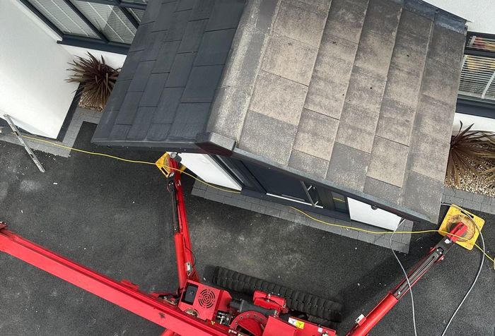 Aerial view of a house roof with a red lift platform beside it and yellow safety anchors at the corners