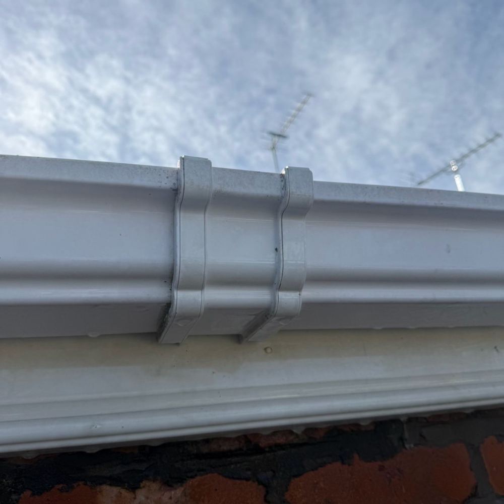 Close-up of a white gutter joint on a brick wall against a blue sky.
