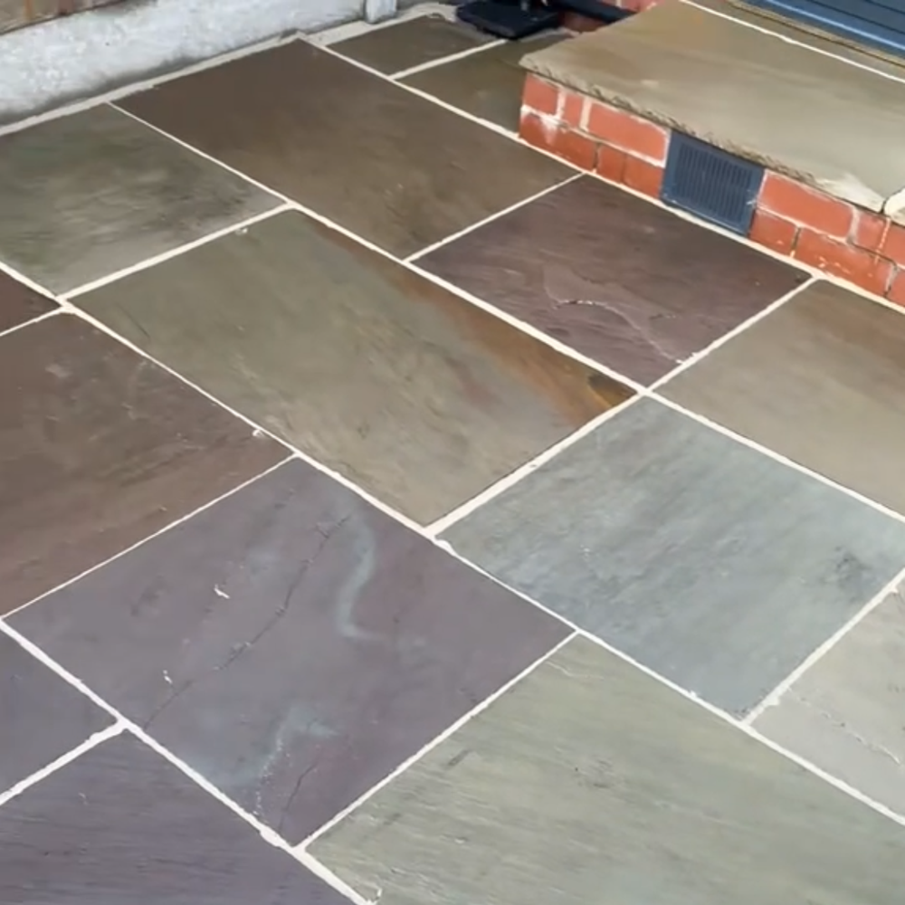 Stone patio tiles with white grout beside a red brick step and gray concrete edge