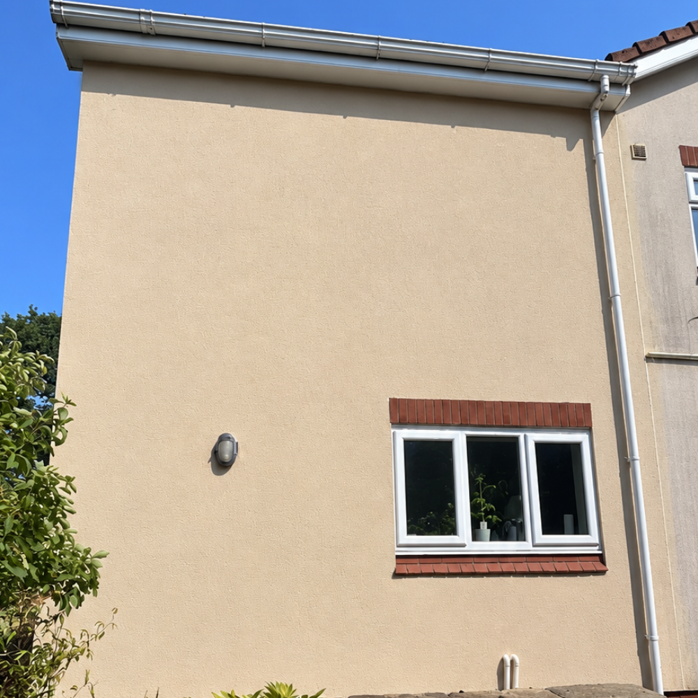 Beige house exterior with a small white-framed window under a blue sky