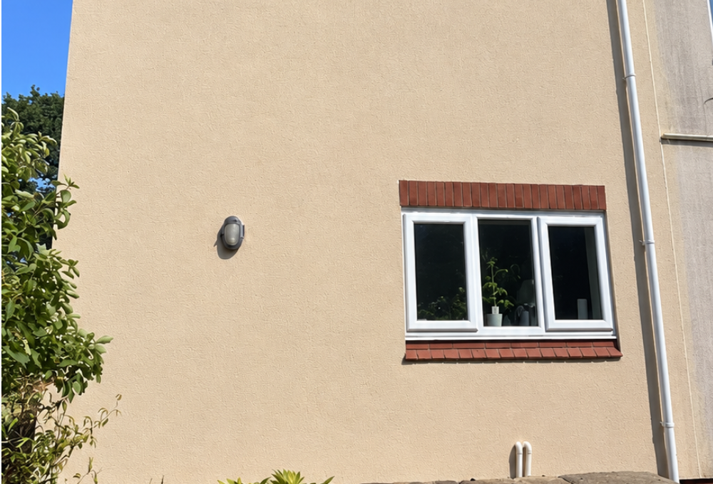 Beige building wall with a small window and wall light in bright sunlight