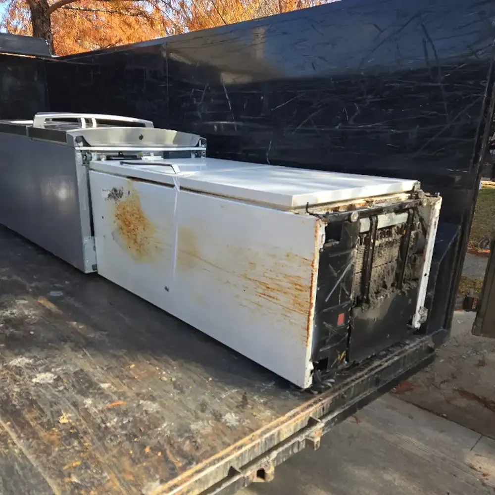 Damaged white commercial freezer units on a flatbed truck, with rust stains and missing front panels
