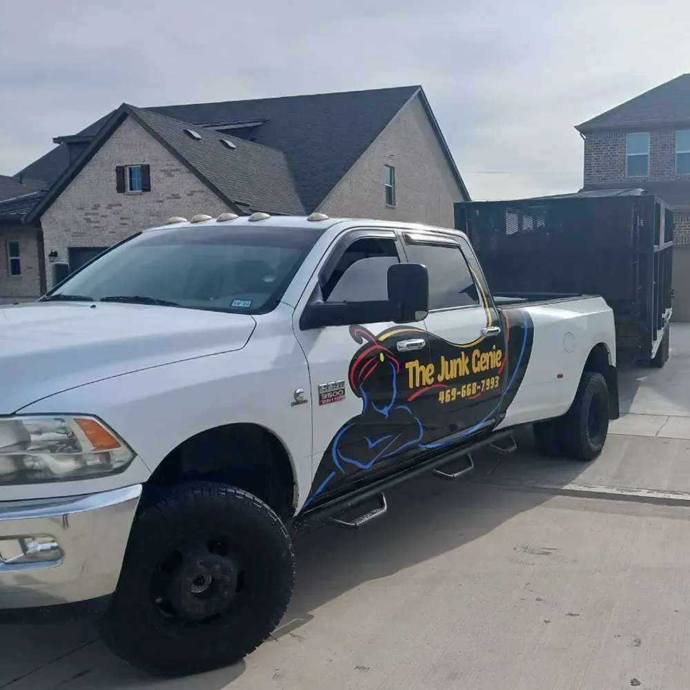 White pickup truck with “The Junk Guys” logo parked in a suburban driveway beside a black trailer.