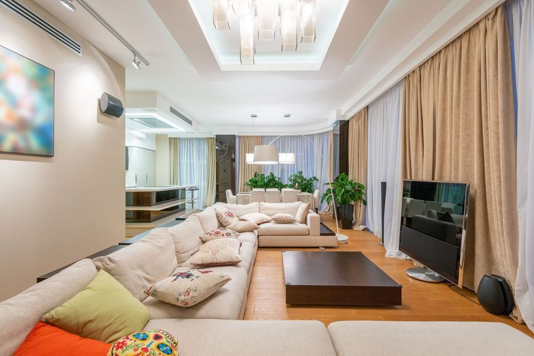 Bright modern living room with beige sofas, a wooden coffee table, TV, and floor-to-ceiling curtains