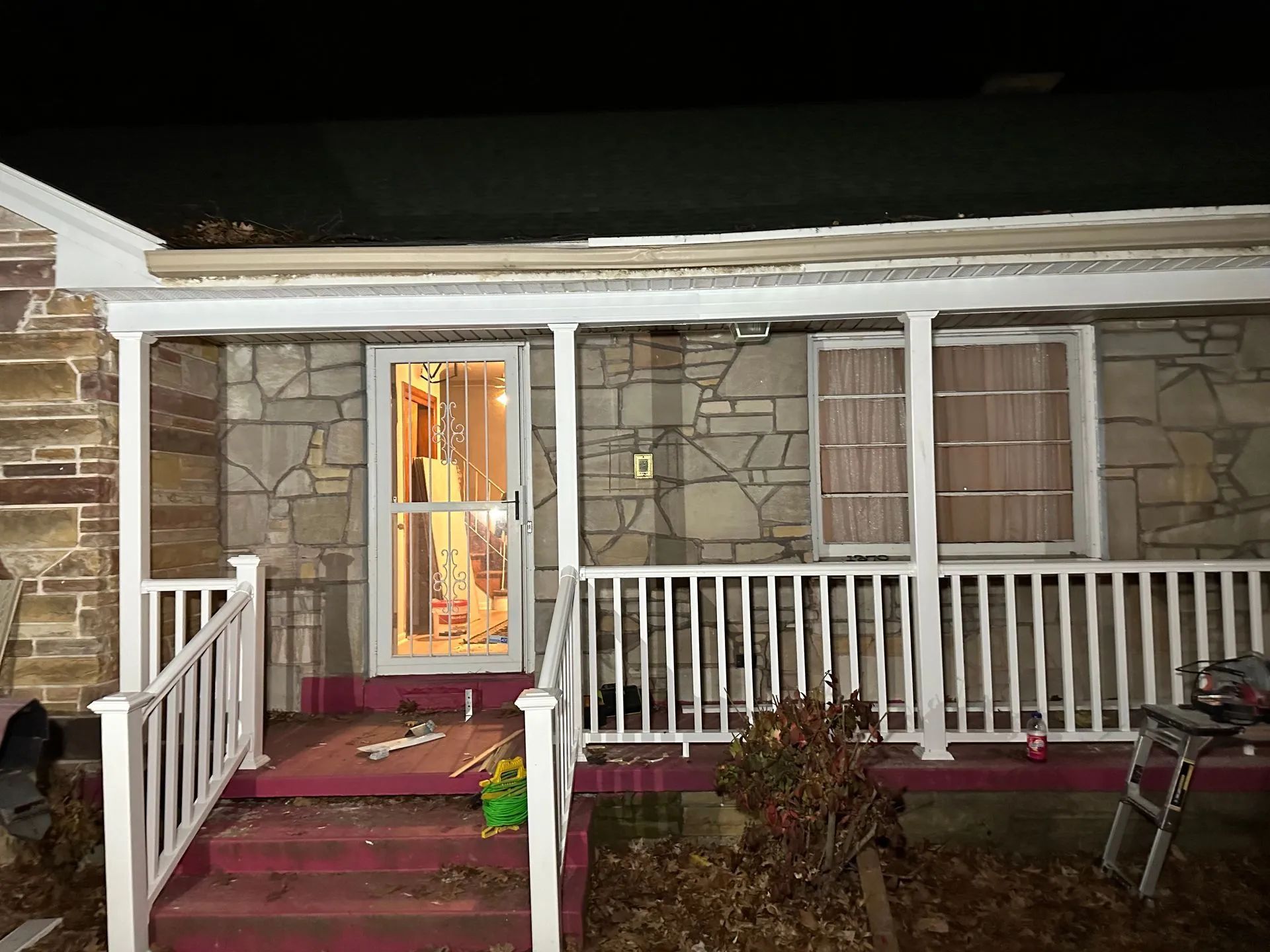 A house with a porch and stairs is lit up at night.