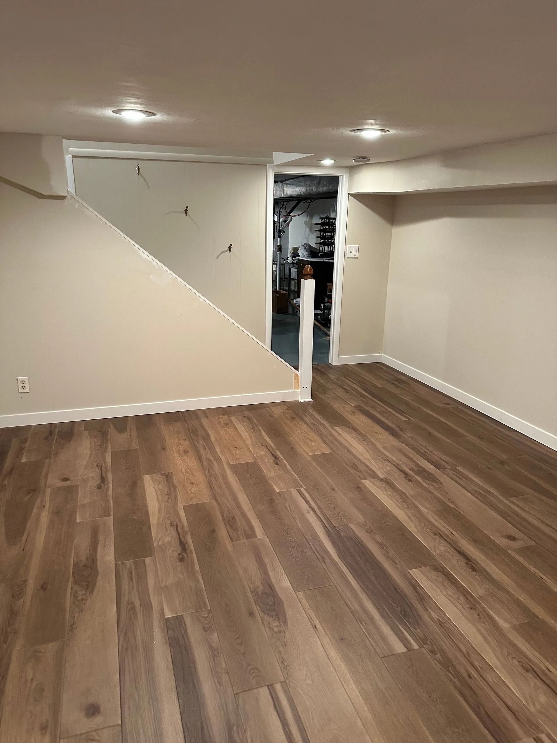 An empty basement with hardwood floors and white walls.