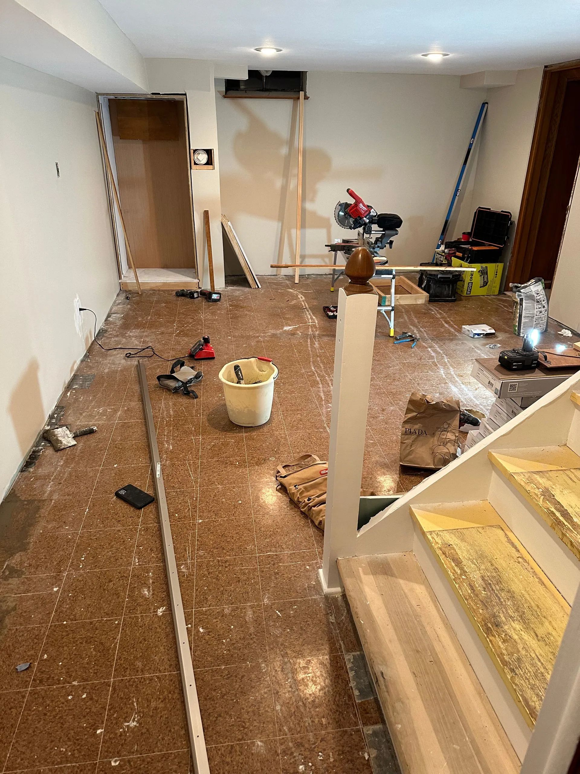 A room with stairs and a bucket on the floor.