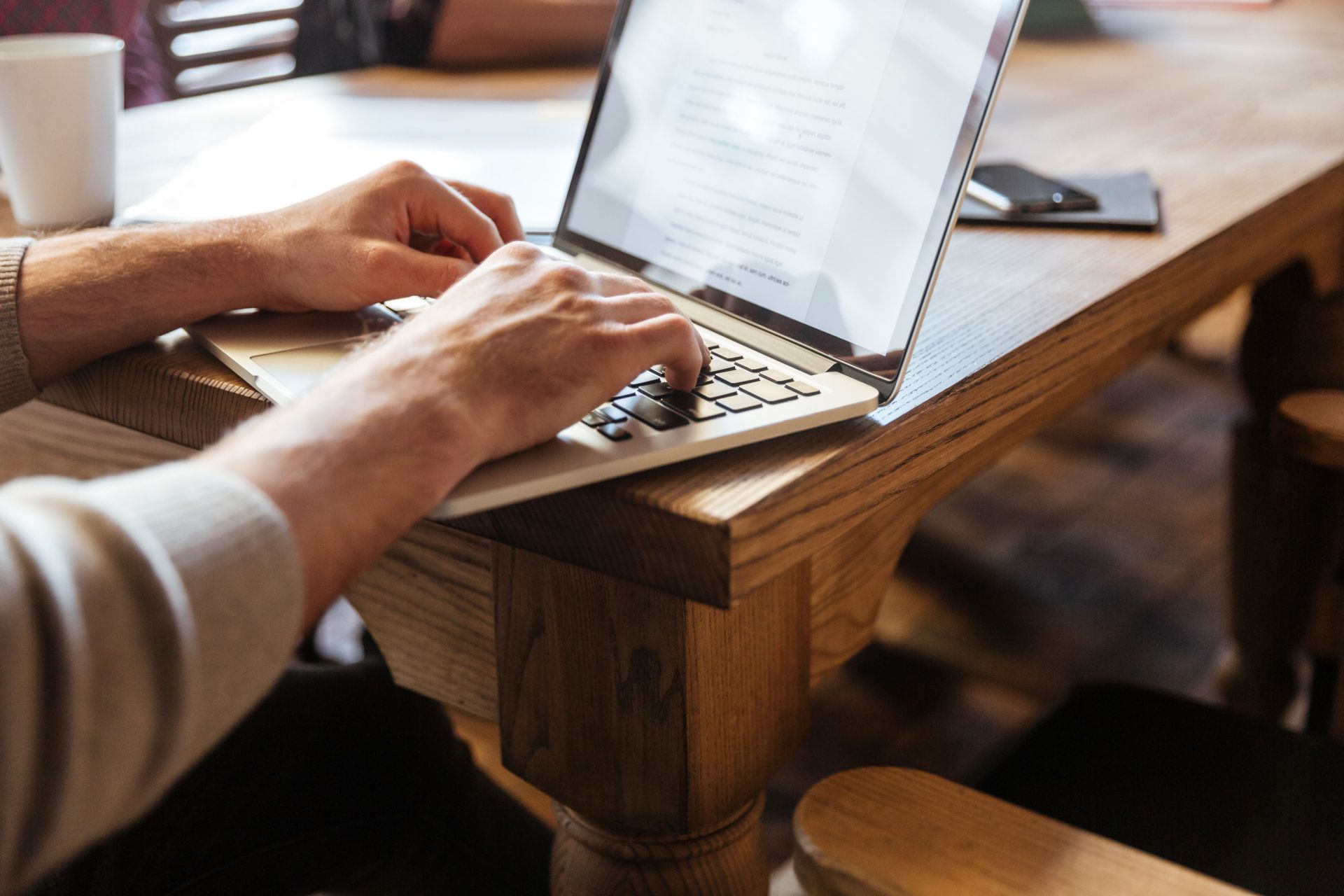 Hands typing on a laptop computer placed on a wooden table.