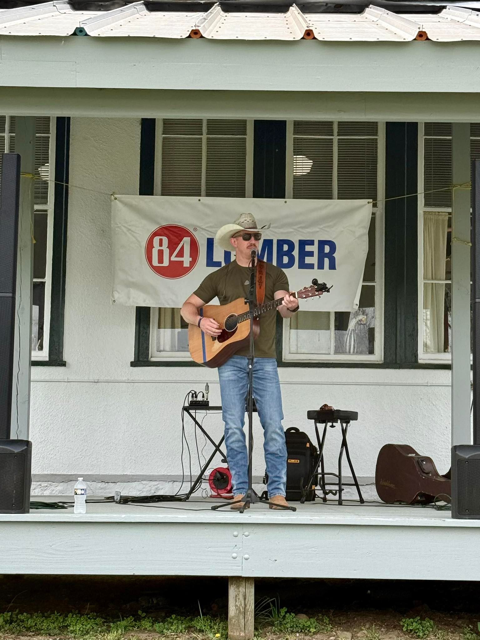Musician playing acoustic guitar on an outdoor stage in front of a Lumber banner
