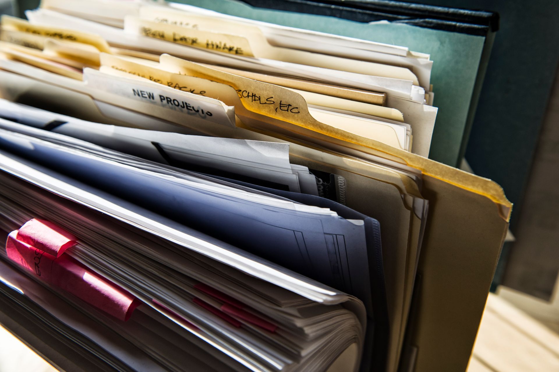 A close-up view of organized file folders in a drawer, with a prominent red clip on the front binder.
