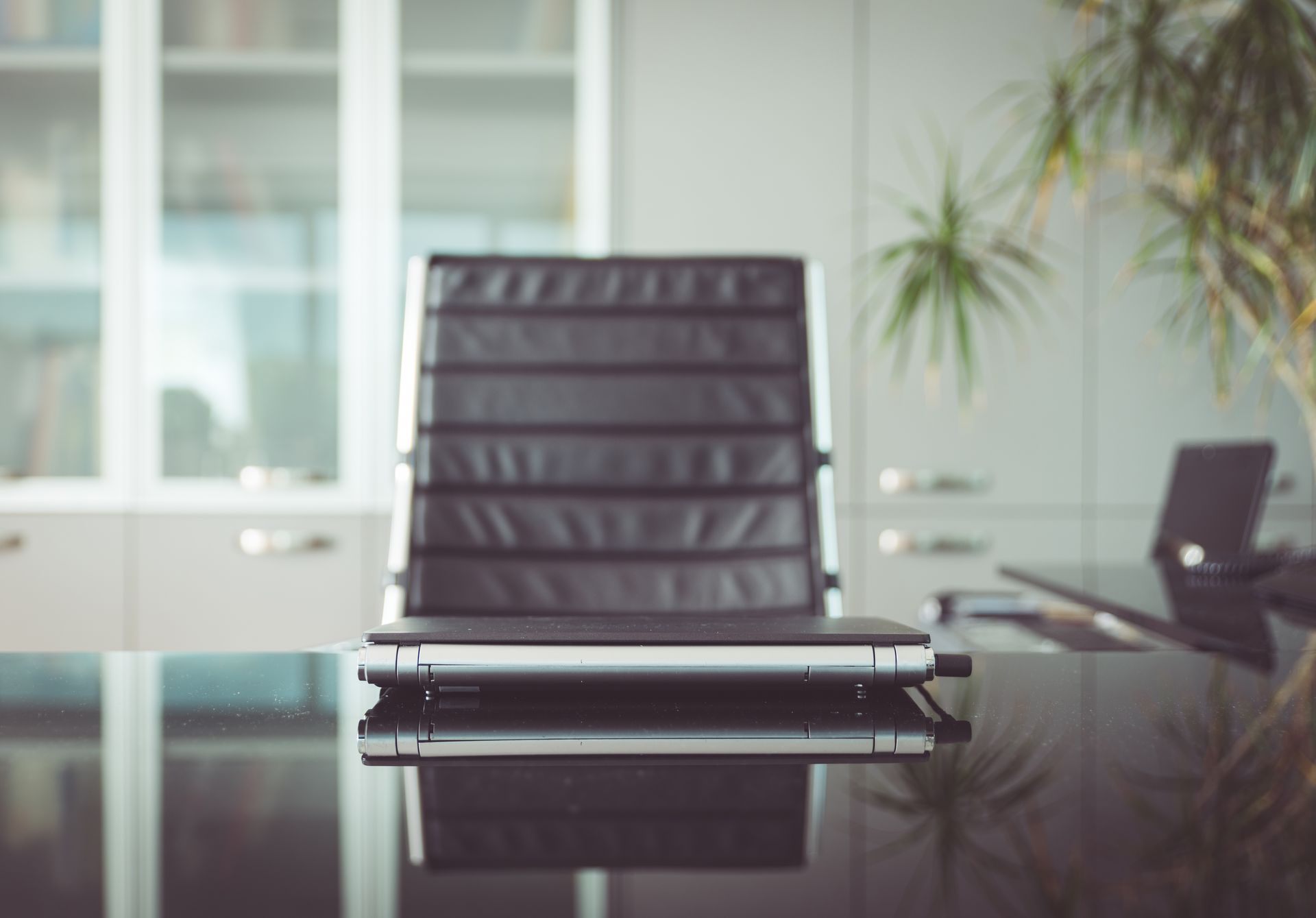 A sleek black office chair positioned on a glossy, reflective desk in a brightly lit, modern office setting.
