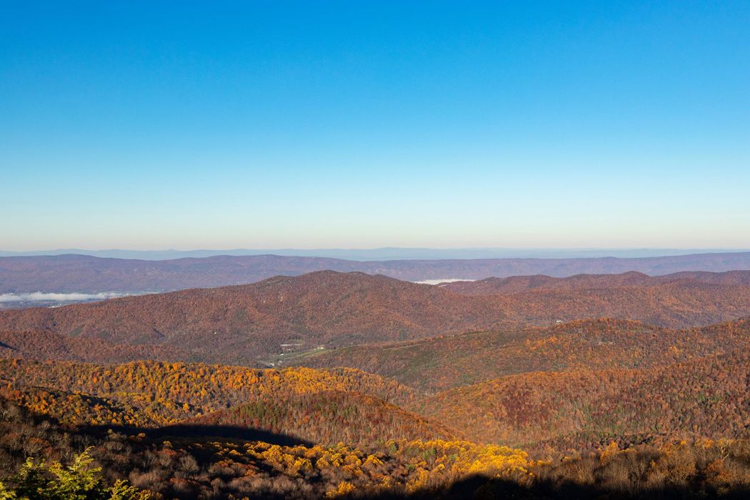 A vast, autumnal mountain landscape under a clear, bright blue sky with hints of morning mist in the valley.