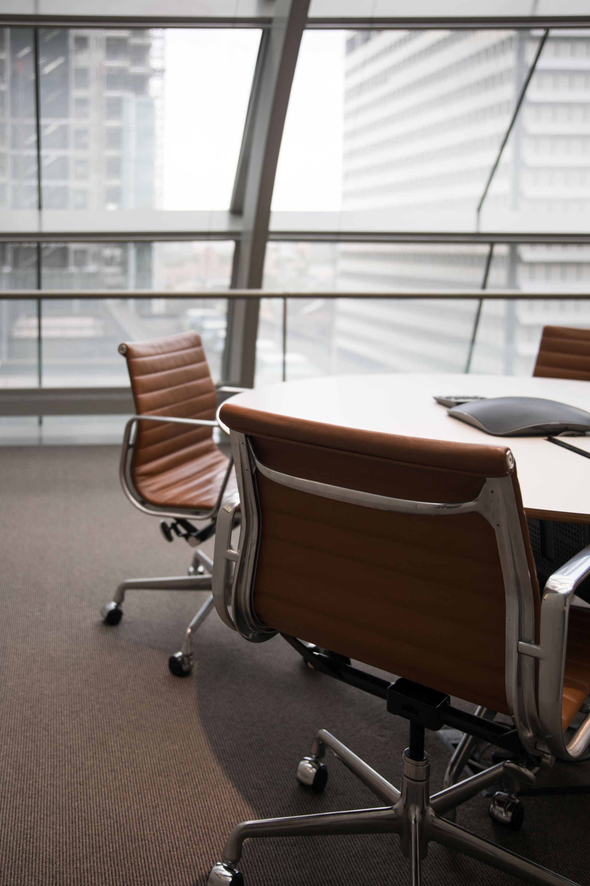 Modern conference room with tan leather chairs arranged around a circular table in front of large windows.