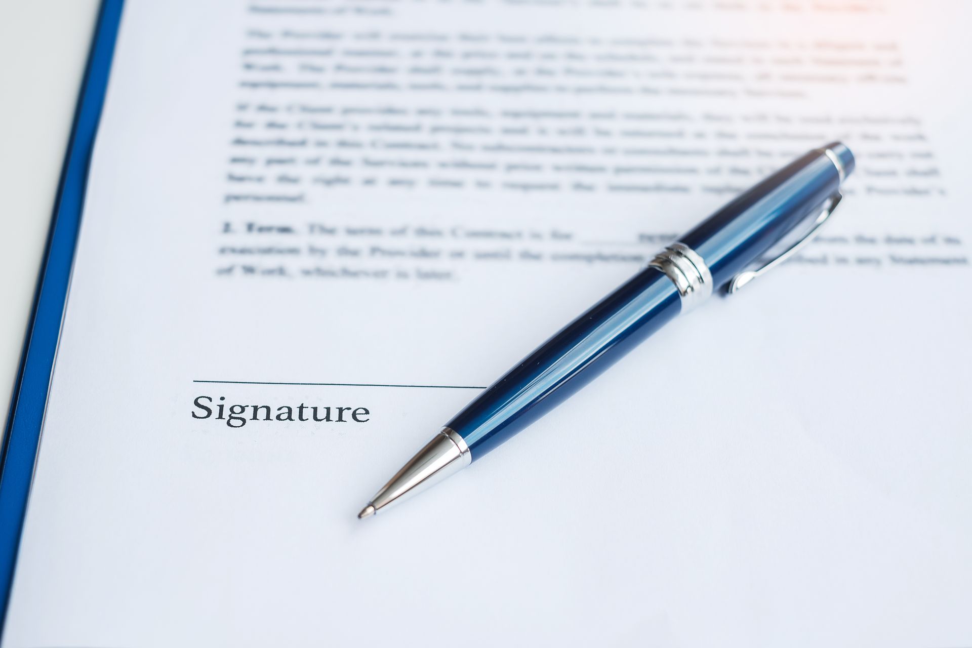 A sleek blue ballpoint pen rests diagonally across a white contract document, positioned just above a signature line.