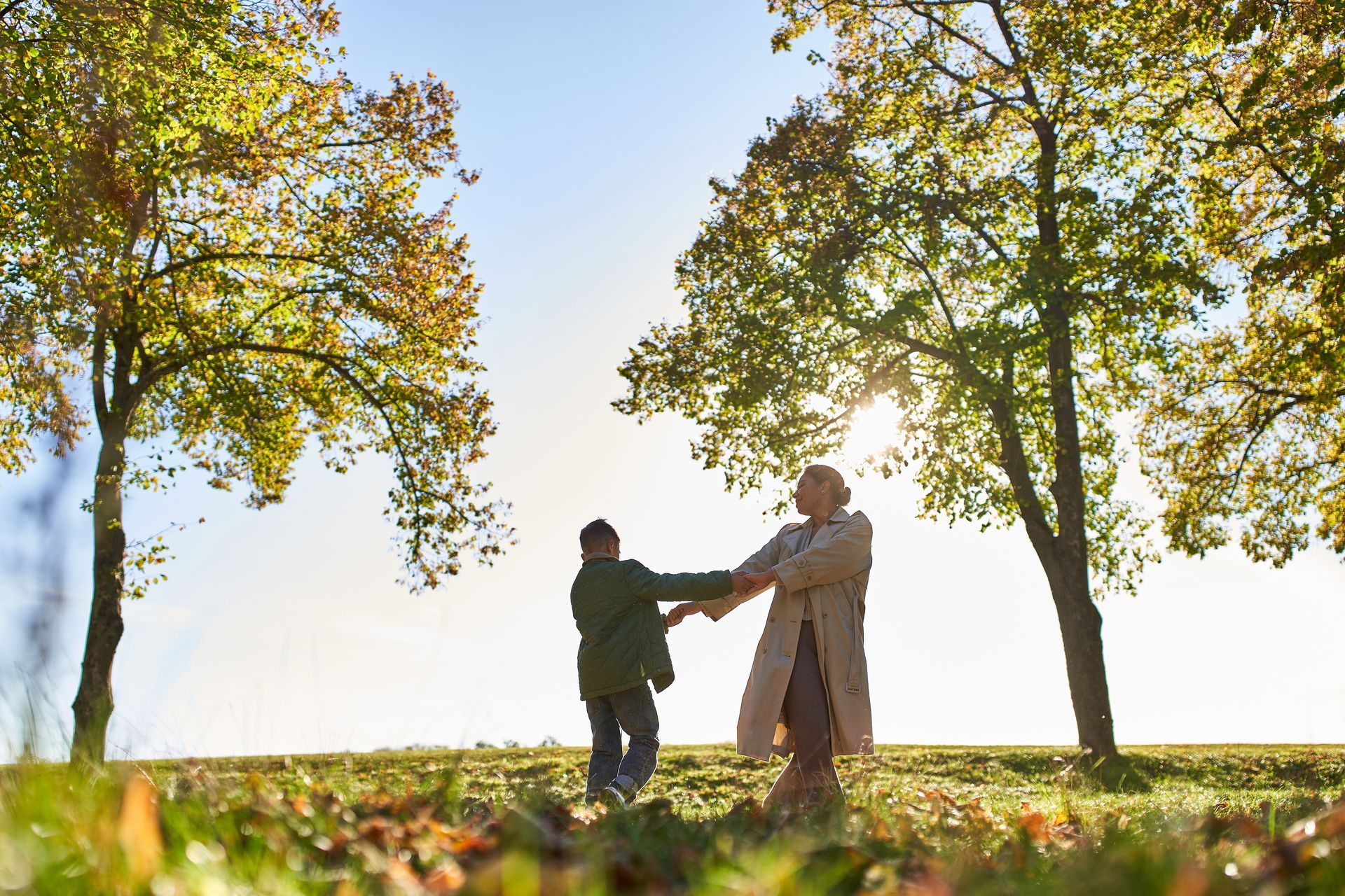 Two people holding hands and dancing in a sunlit field surrounded by autumn trees.
