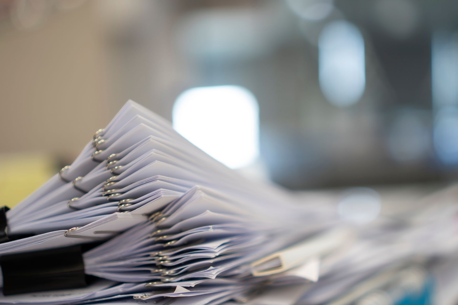 A stack of white paper documents, secured with silver staples and a black binder clip, resting on a desk.