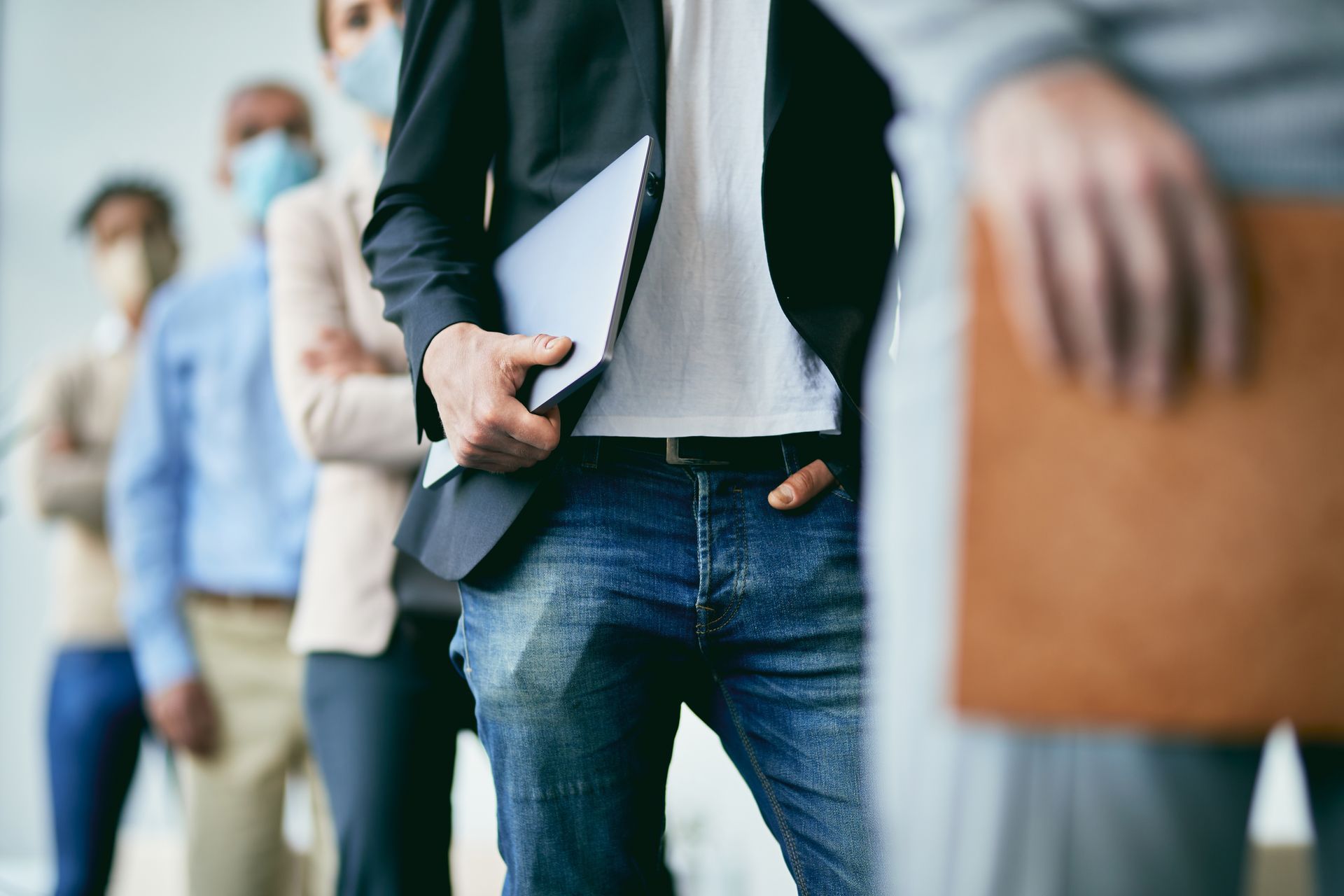 A line of people in business casual attire wearing face masks while standing in an office hallway.