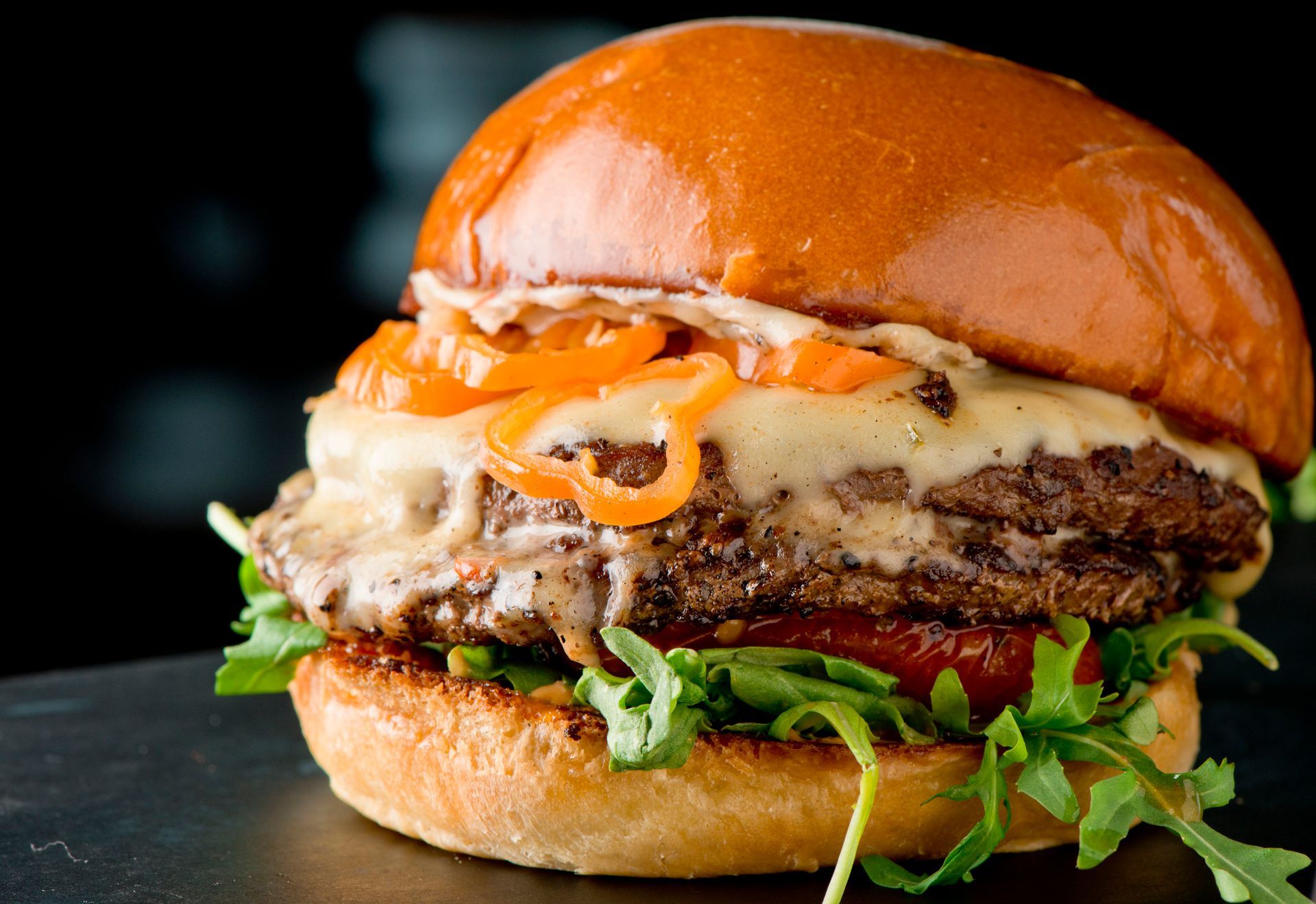 Burger with melted cheese, caramelized onions, arugula, and tomato on a toasted bun.