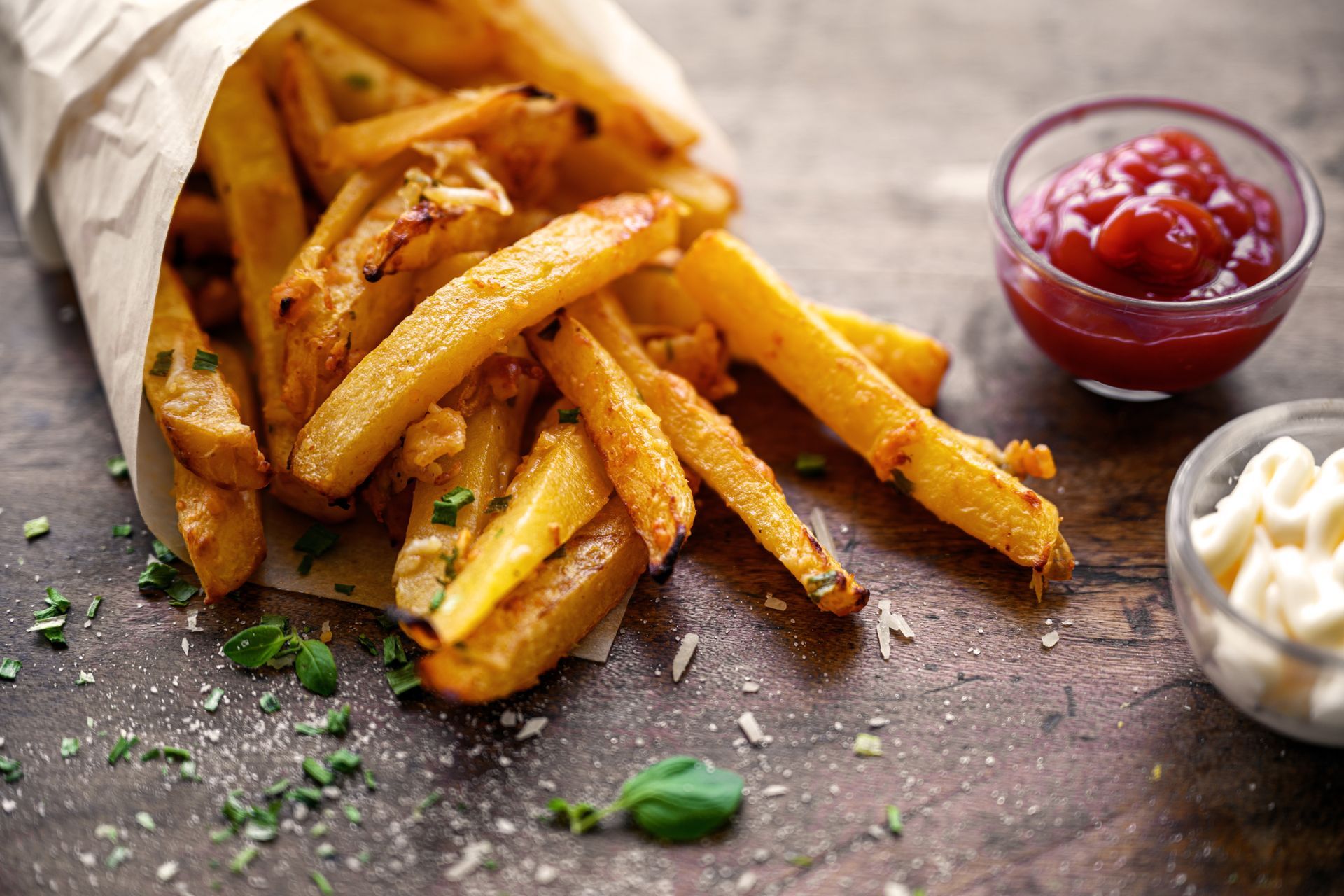 Golden french fries in paper cone, with ketchup and mayo on wooden table.