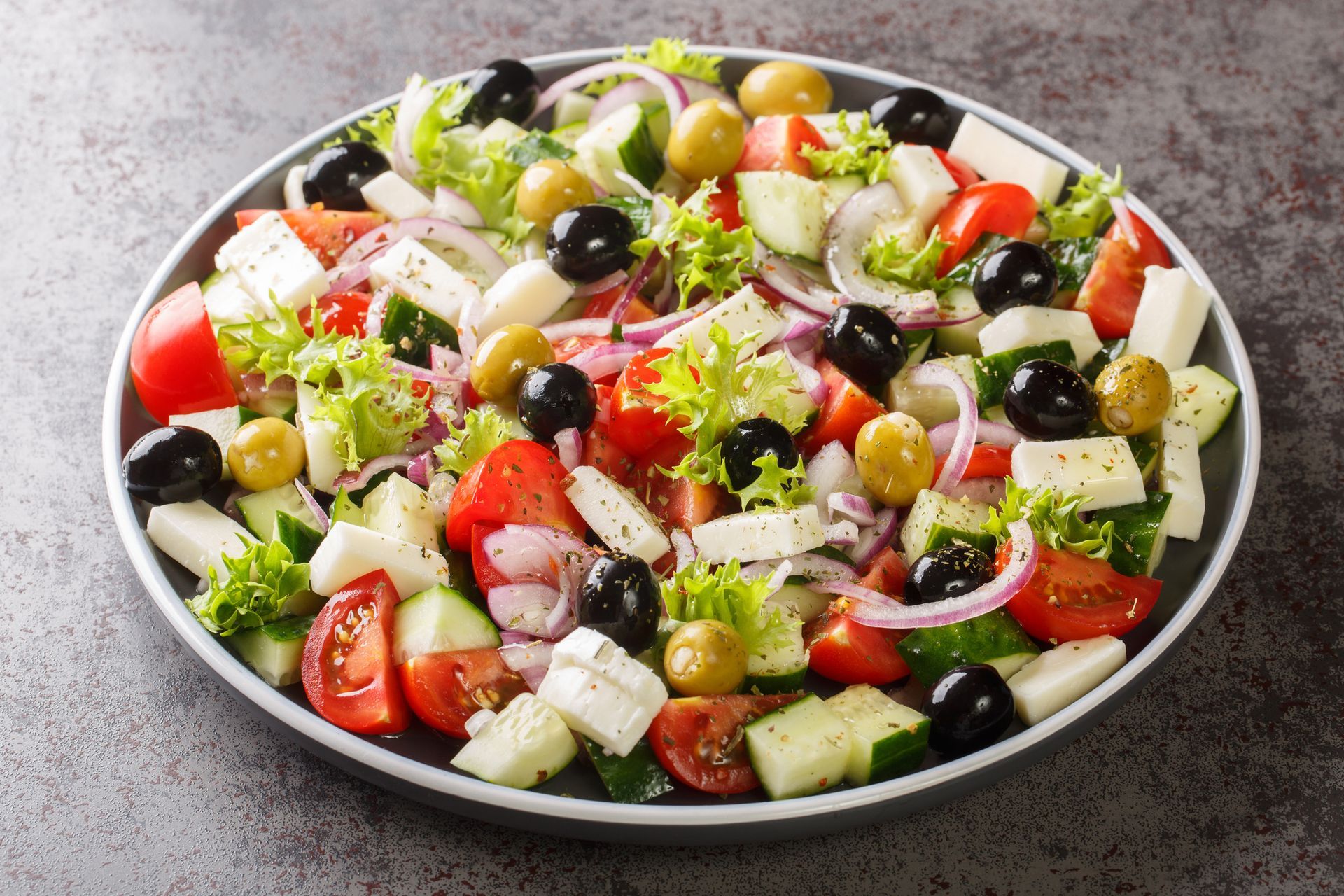 Greek salad with tomatoes, cucumbers, onions, olives, and feta cheese in a grey bowl.