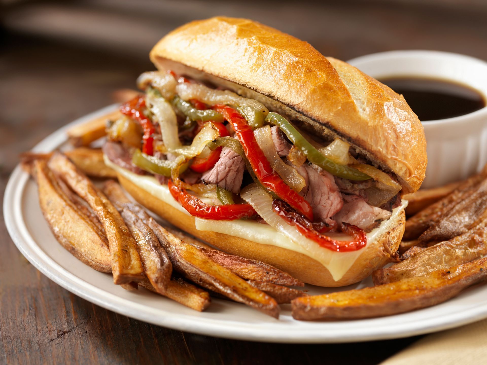 Philly cheesesteak sandwich with peppers and onions, served with fries and dipping sauce.