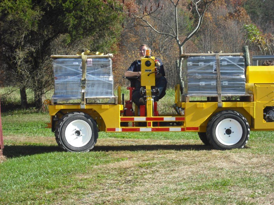 Yellow work vehicle carrying stacked clear containers. A person is seated and operating it outdoors.