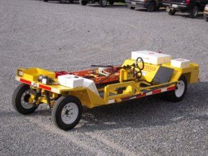 Yellow aircraft tow tractor on a gravel surface, with white tires and safety markings.