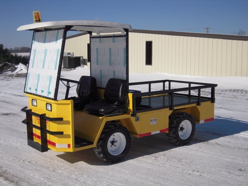 Yellow utility vehicle with seats, bed, and roof, parked on snowy ground.
