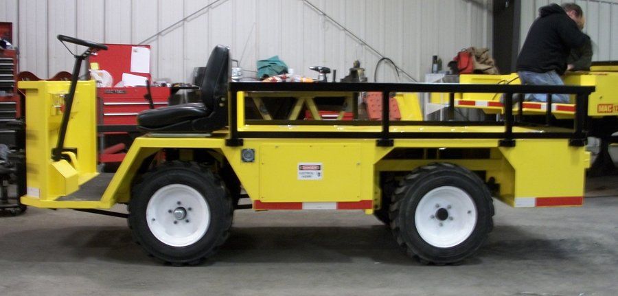 Yellow utility vehicle with a black frame and white wheels, in a garage with a person working on it.