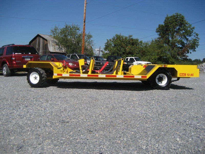 Yellow, industrial trailer with large tires parked on gravel, with vehicles and trees in background.