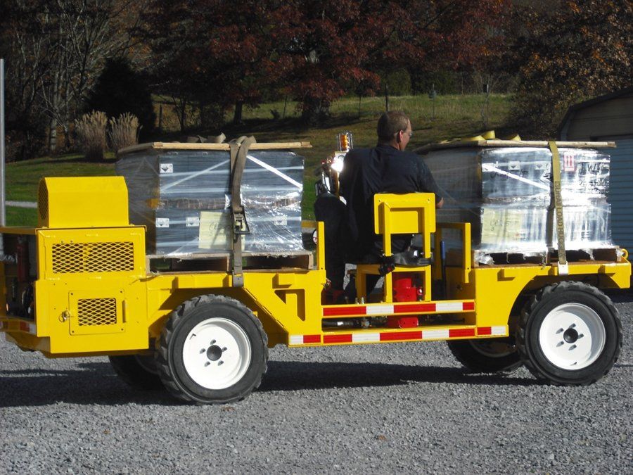 Yellow industrial cart with driver transporting stacked cargo outdoors.