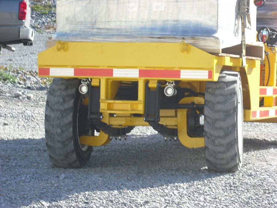 Rear view of yellow industrial vehicle with large tires, red and white reflective strip, and lights.