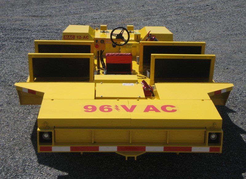 Yellow industrial railcar with steering wheel, 96V AC marking, on gravel.