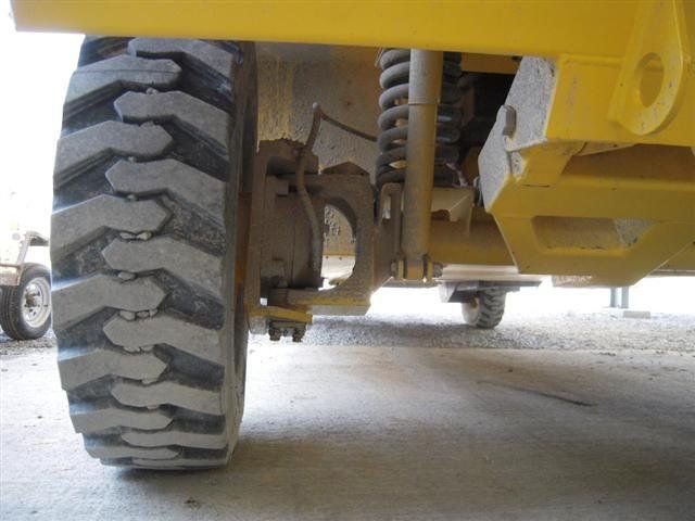 Yellow construction vehicle's tire and suspension, close up. Dirt and worn tread visible.