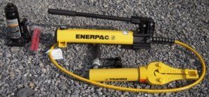A set of yellow Enerpac hydraulic tools on a gravel surface. Includes a jack, pump, and spreader.