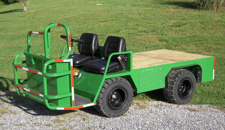 Green utility vehicle with two black seats and a flatbed, parked on grass.