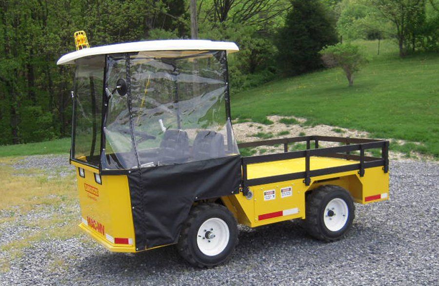 Yellow utility cart with enclosed cab and cargo bed on gravel driveway.